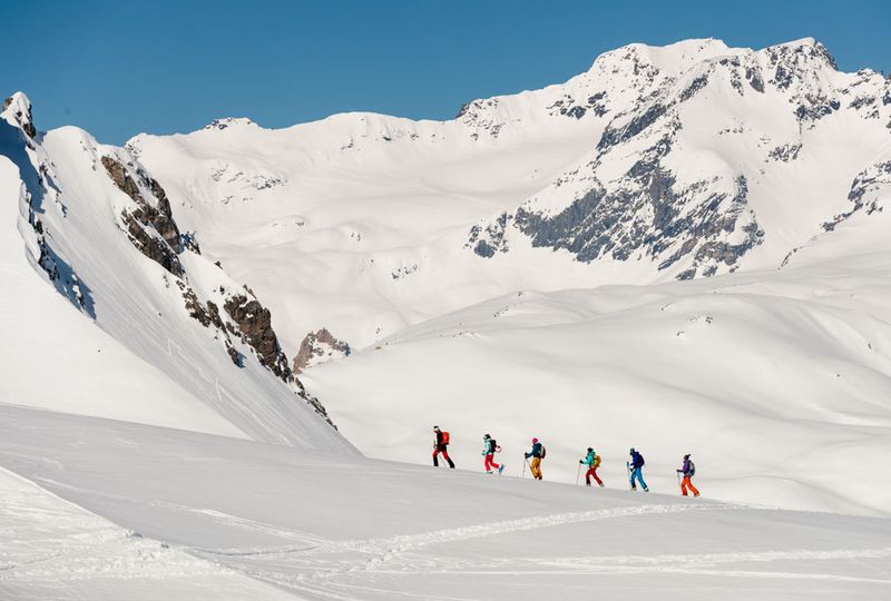 a line of ski tourers head uphill in the backcountry - deep snow is everywhere